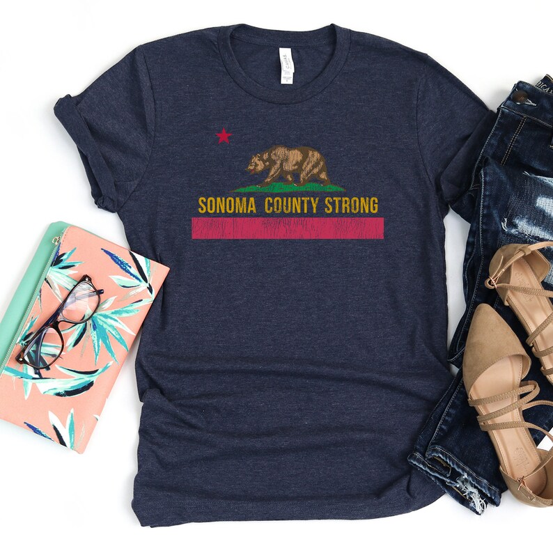 May include: A navy blue t-shirt with a distressed red, white, and yellow graphic of the California state flag with a bear and the text "Sonoma County Strong".