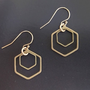 May include: A pair of gold-toned earrings with a geometric hexagon design. The earrings feature two concentric hexagons, creating a layered effect.