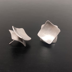 May include: A pair of silver earrings with a geometric design. The earrings are made of two overlapping squares, creating a three-dimensional effect.
