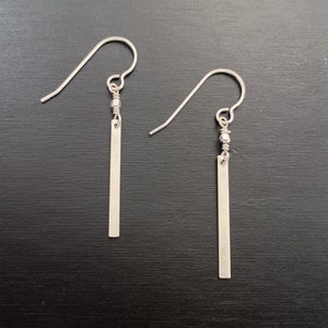 May include: A pair of silver dangle earrings with a long, thin, rectangular bar pendant.