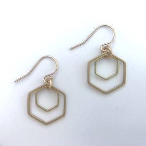 May include: A pair of gold-toned earrings with a double hexagon design. The earrings are made of metal and have a simple, geometric shape.