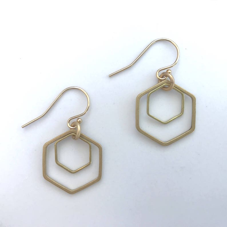 May include: A pair of gold-toned earrings with a double hexagon design. The earrings are made of metal and have a simple, geometric shape.