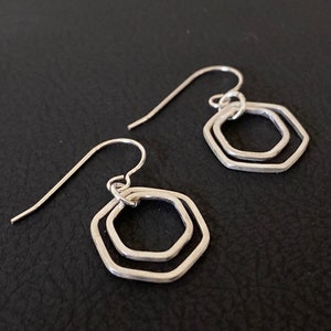May include: A pair of silver earrings with a double hexagon design. The earrings are made of a thin wire and have a simple, modern style.