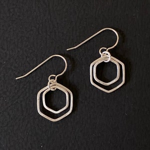 May include: A pair of silver earrings with a double hexagon design. The earrings are simple and elegant.