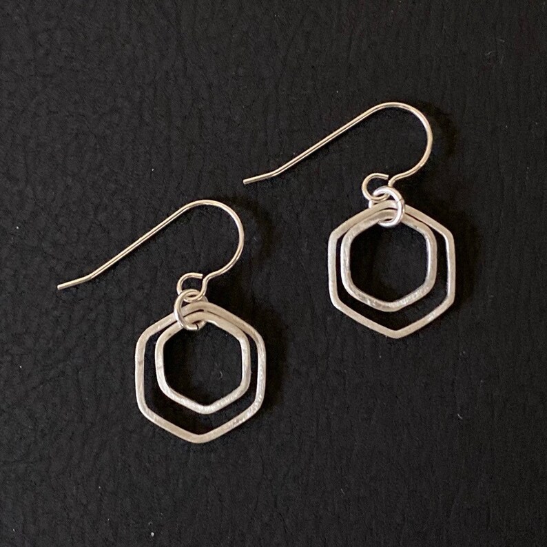 May include: A pair of silver earrings with a double hexagon design. The earrings are simple and elegant.