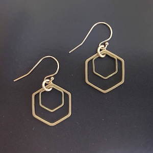 May include: A pair of gold-toned earrings with a geometric hexagon design. The earrings feature two concentric hexagons, creating a layered effect.