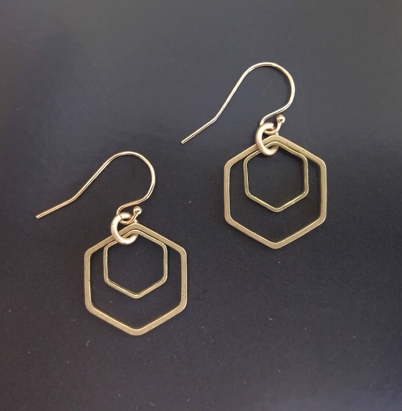 May include: A pair of gold-toned earrings with a geometric hexagon design. The earrings feature two concentric hexagons, creating a layered effect.