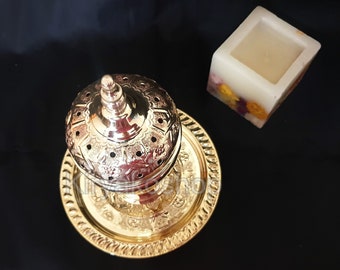 May include: A gold metal incense burner with intricate designs and a round top. The burner is sitting on a matching gold metal tray.