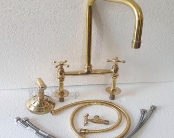 May include: A gold-tone kitchen faucet with two handles and a pull-down sprayer. The faucet has a high arc spout and a traditional design.