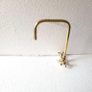 May include: A gold-toned kitchen faucet with a curved spout and two handles. The faucet is mounted on a white wall.