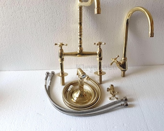 Puede incluir: Un conjunto de grifos y accesorios de cocina de latón. El conjunto incluye un grifo de puente, un grifo de cuello de cisne, un rociador lateral y varias mangueras de conexión. Los accesorios tienen un acabado dorado pulido y detalles de manija en cruz.