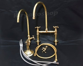 Puede incluir: Un grifo de cocina dorado con dos caños separados y un pulverizador de mano. El grifo tiene un diseño tradicional con manijas en forma de cruz. El grifo se muestra con sus mangueras y accesorios.