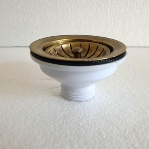 May include: A white plastic sink strainer with a brass strainer basket. The strainer has a threaded bottom for installation.