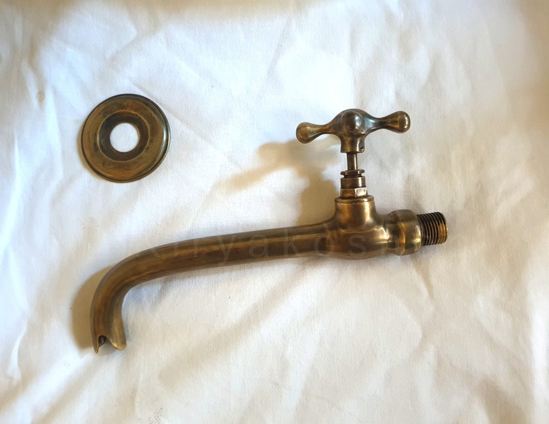 Pu&ograve; includere: Rubinetto in ottone con un becco lungo e una maniglia a forma di croce. Il rubinetto &egrave; fissato a una parete e ha una piastra di copertura rotonda decorativa.