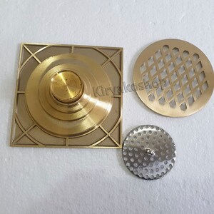 May include: A collection of brass and silver-toned metal drain covers. The square brass cover has a central knob and geometric design. A round brass cover features a diamond pattern, and a smaller, perforated silver-toned cover is also included.