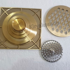 May include: A collection of brass drain covers and components. Includes a square drain cover with a central circular design, a round cover with a diamond pattern, and a smaller, perforated metal disc.