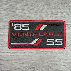 May include: Black rectangular patch with red border featuring the text "'85 MONTE CARLO SS" in white and red. The design includes red and white accent stripes. The patch is likely for a car enthusiast.