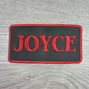 May include: Embroidered patch with the name "JOYCE" in red capital letters on a black rectangular background. The patch has a red border and is likely designed to be sewn or ironed onto fabric.