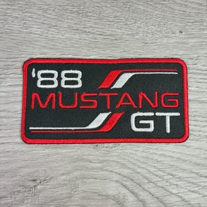 May include: Embroidered patch featuring the text "'88 MUSTANG GT" in white and red on a black background. The patch has a red border and a design with red and white stripes.