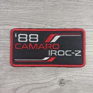 May include: A rectangular embroidered patch with a black background and a red border. The text '88 CAMARO' appears in white and red, with 'IROC-Z' in white. Red and white horizontal lines accent the design, creating a bold, automotive-themed graphic.