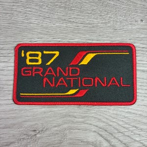 May include: Rectangular patch with a black background and a red border. The patch features the text "'87 GRAND NATIONAL" in yellow and red, with a stylized design. The patch is likely for a car enthusiast.