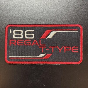 May include: A rectangular embroidered patch with a black background and a red border. The text '86' appears in white, followed by the red text 'REGAL T-TYPE'. The design includes stylized red and white graphic lines that frame the lettering.