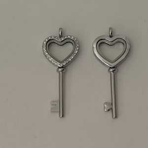 Peut inclure: Deux pendentifs en forme de clé argentés avec des ouvertures en forme de cœur. Un pendentif a un cœur transparent avec une bordure de petits strass. L'autre pendentif a un cœur transparent avec une bordure lisse.