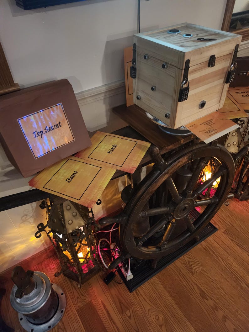 Puede incluir: Una caja de madera con m&uacute;ltiples cerraduras de combinaci&oacute;n, un tim&oacute;n y una linterna. La caja tiene un acabado de madera clara y tiene forma de cubo. El tim&oacute;n es de color marr&oacute;n oscuro. La linterna es ornamentada con un marco de metal y est&aacute; iluminada con un brillo c&aacute;lido. Las palabras "Top Secret" son visibles.