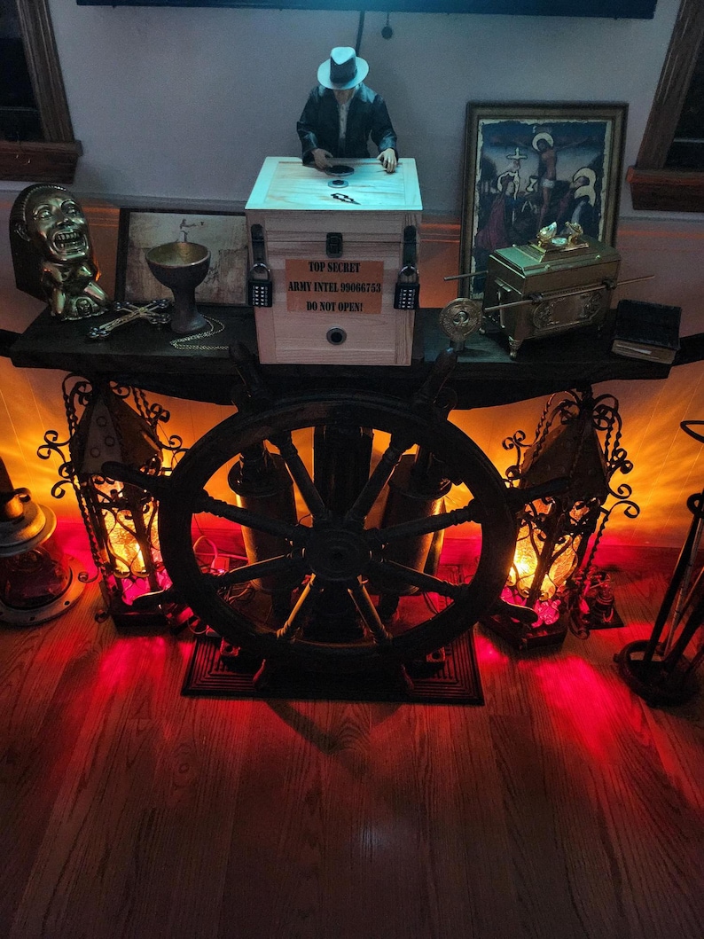 Puede incluir: Una caja de madera con la etiqueta "TOP SECRET" con una figura encima, flanqueada por candados. La exhibici&oacute;n incluye un tim&oacute;n de barco, faroles y varios objetos decorativos. El texto "ARMY INTEL 09006753 DO NOT OPEN!" es visible en la caja.