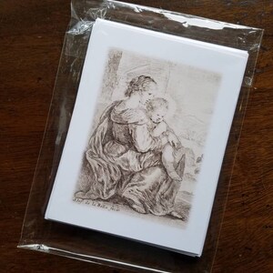 May include: A stack of white art prints featuring a black and white etching of a woman holding a child. The prints are sealed in a clear plastic sleeve. The artwork is signed "Stef. de la Bella fecit."
