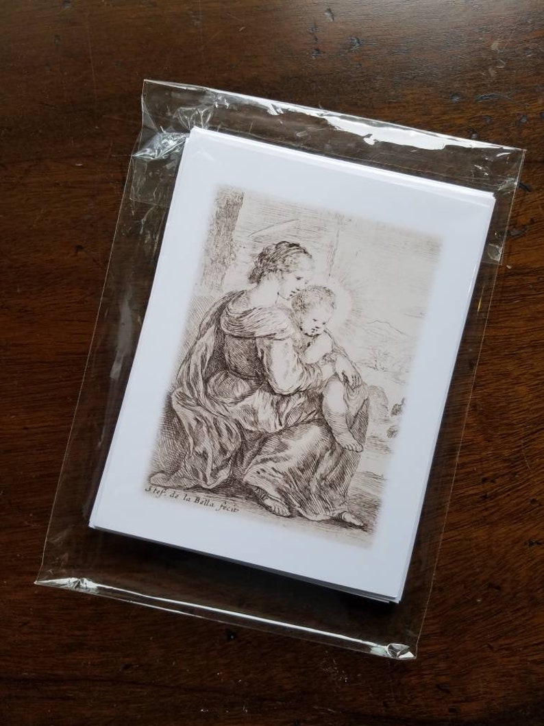 May include: A stack of white art prints featuring a black and white etching of a woman holding a child. The prints are sealed in a clear plastic sleeve. The artwork is signed "Stef. de la Bella fecit."