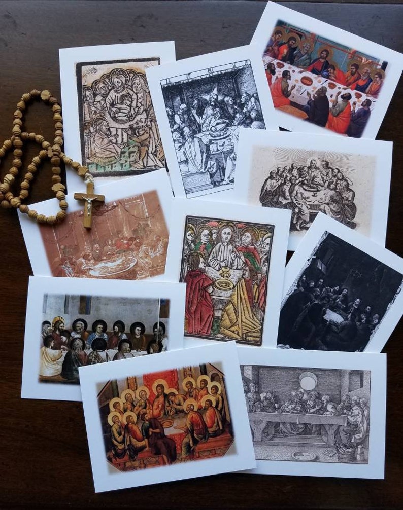 May include: A selection of square greeting cards displaying religious art, illustrating biblical scenes. The cards showcase diverse styles, including colour paintings and monochrome etchings. A wooden rosary with a cross is also visible.