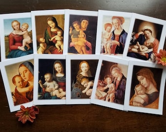 May include: A set of art prints displaying Renaissance paintings of the Madonna and Child. Each print presents a unique portrayal of the Virgin Mary with the infant Jesus, in diverse poses and colour schemes. The prints are arranged on a dark wooden surface.