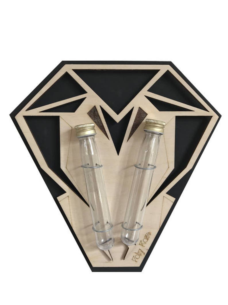 Op de afbeelding: Een houten diamantvormige wandbevestiging met twee glazen reageerbuizen en gouden deksels. De bevestiging is zwart met een houtnerfpatroon en de tekst "Poly Rare" is onderaan gedrukt.