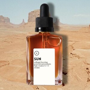 May include: A square amber-colored bottle with a black dropper top, labeled "SUN" in white, sits against a desert landscape. The label also lists "collagen boosting" and "powerful antioxidants." The words "elemental beauty" are at the bottom.