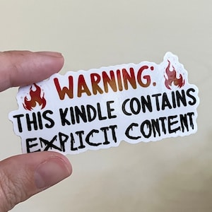 May include: A white sticker with black text that reads "WARNING: THIS KINDLE CONTAINS EXPLICIT CONTENT". The sticker has two red and orange flames on either side of the text.