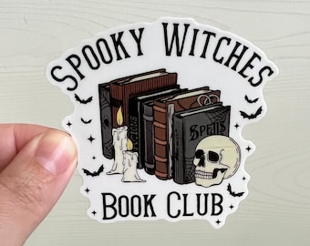 May include: A white sticker with the text "Spooky Witches Book Club" in black lettering. The sticker features a stack of books with the words "Spells" and "Potions" on the spines, two lit candles, and a skull.