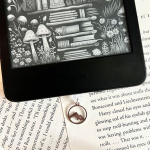 May include: A close-up of a black and white e-reader with a mountain-shaped bookmark. The e-reader is on a white surface with text.