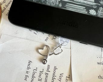 May include: A silver stethoscope charm with a heart-shaped end attached to a black Kindle e-reader.