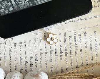 May include: A white daisy-shaped bookmark with a gold outline and a smiley face. The bookmark is attached to a clear plastic string.