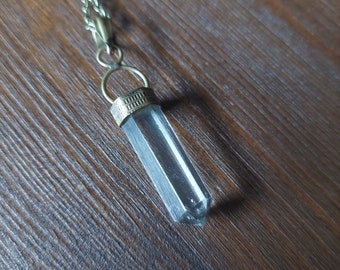 May include: A clear quartz crystal pendant on a brass chain. The crystal is faceted and has a pointed tip. The chain is braided and has a simple clasp.