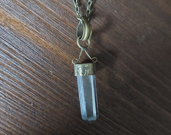 May include: A clear quartz crystal pendant necklace with a gold-toned chain and a detailed metal setting.