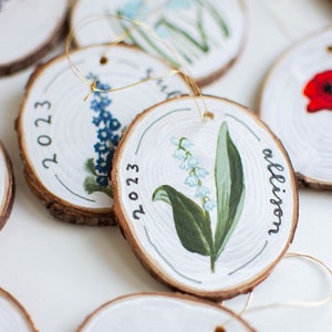 May include: A set of round wood ornaments with painted floral designs and the year 2023. One ornament has the name "Allison" written on it.