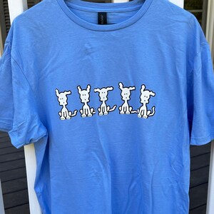 May include: A light blue t-shirt with a graphic of five white cartoon dogs sitting in a row.