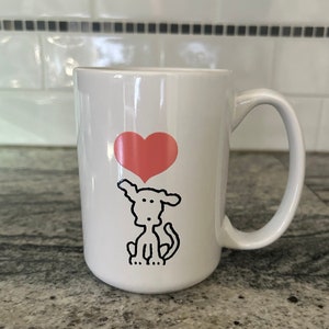Puede incluir: Taza de café de cerámica blanca con un dibujo de línea negra de un perro con un corazón rosa encima.
