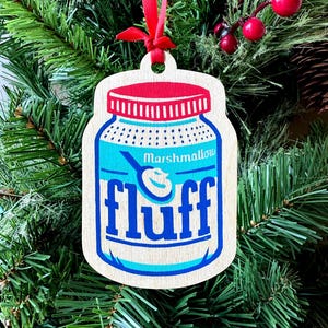 May include: Wooden Christmas ornament shaped like a jar of Marshmallow Fluff. The jar is blue with a red lid and the word "fluff" in large blue letters. A red ribbon is attached for hanging.