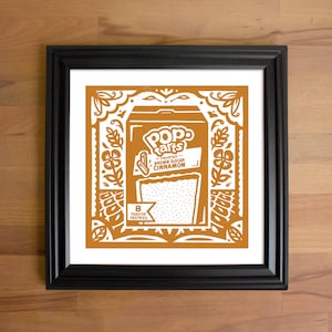 May include: Framed art print featuring a Pop-Tarts box design in shades of brown and white. The artwork includes the Pop-Tarts logo, flavor details, and decorative floral and scrollwork borders. The print is in a black frame.