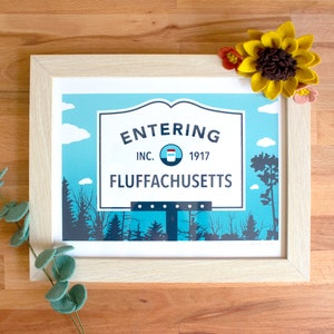 Puede incluir: Impresión artística enmarcada con un letrero que dice "ENTERING FLUFFACHUSETTS INC. 1917". La obra de arte está en un marco de madera clara, con un cielo azul, nubes blancas y una escena de bosque. Flores decorativas de fieltro están colocadas en el marco.