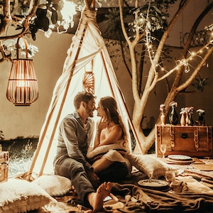 Puede incluir: Una escena rom&aacute;ntica al aire libre por la noche, con una pareja dentro de una peque&ntilde;a tienda tipi. La tienda est&aacute; iluminada con luces c&aacute;lidas, y la pareja est&aacute; cerca. Linternas decorativas y luces de hadas contribuyen al ambiente.