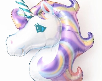 May include: A large, foil unicorn balloon in the shape of a unicorn head. The unicorn has a white face, blue eyes, and a striped horn. The mane and neck are a mix of pastel colors, including purple, pink, and yellow.